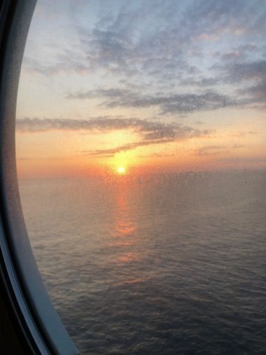 Blick aus dem Bullauge einer Außenkabine auf dne Sonnenaufgang am Horizont