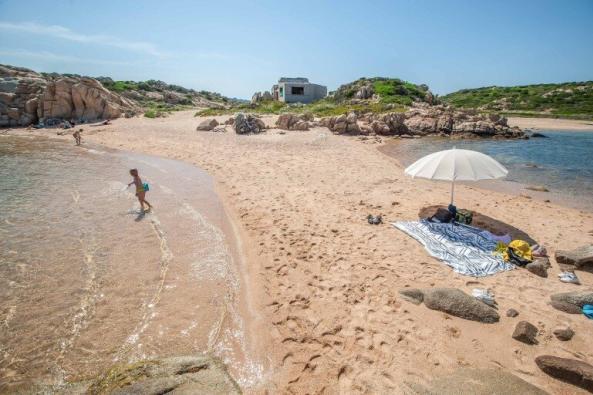 Strand auf La Maddalena gegenüber dem Campingplatz mit Schirm, Handtüchern und verfallenem Haus