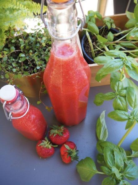 zwei Flaschen selbstgemachter Erdbeerlimes mit ein paar Erdbeeren davor Totale