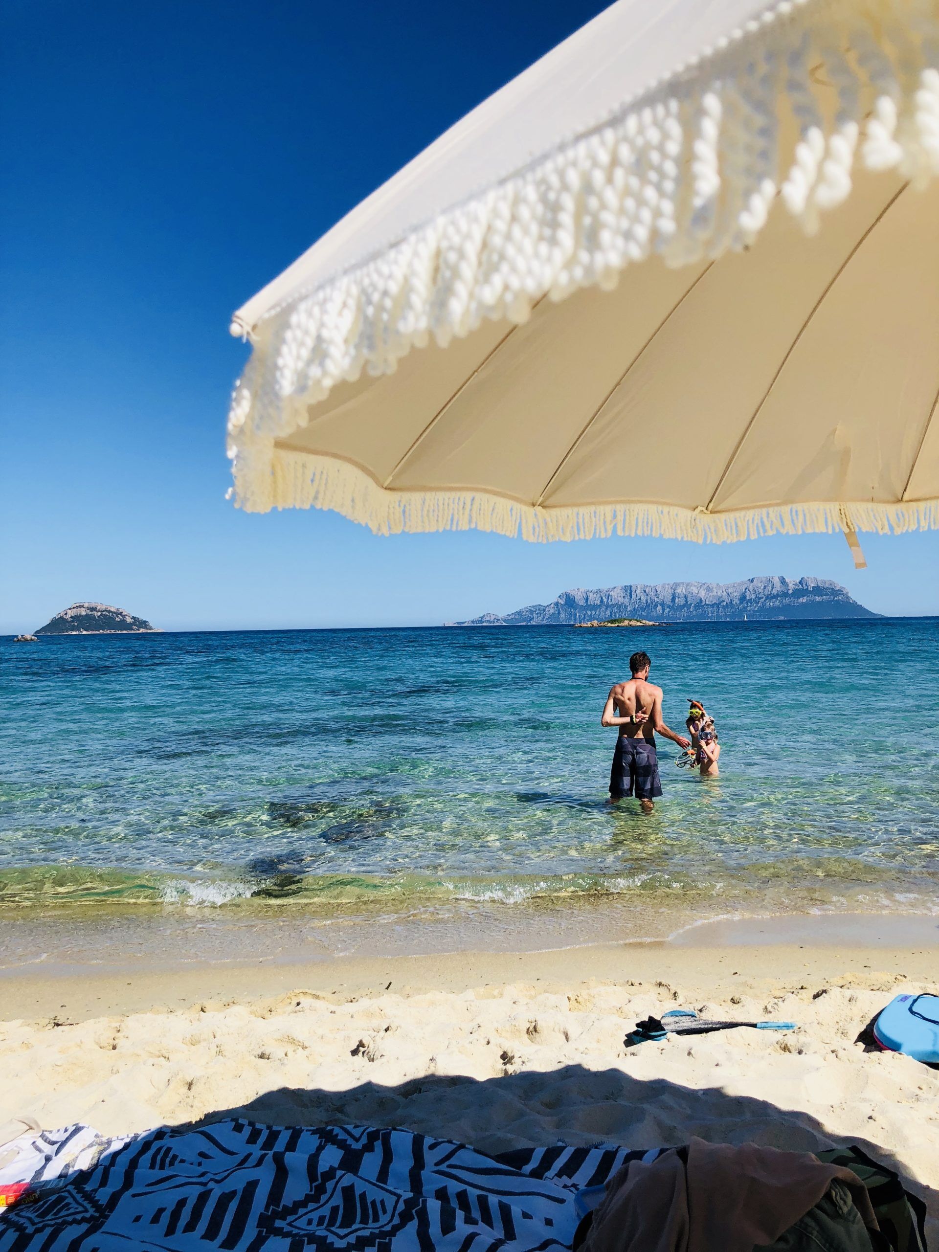 Meer und creme farbener Sonnenschirm am Strand im Hintergrund ein Berg