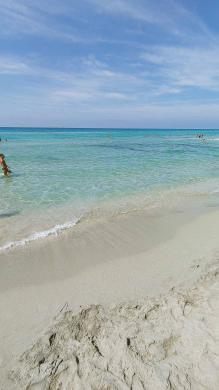Mann geht durch klasklares türkises Wasser am Strand von Riva di Ugento - Camping in Apulien