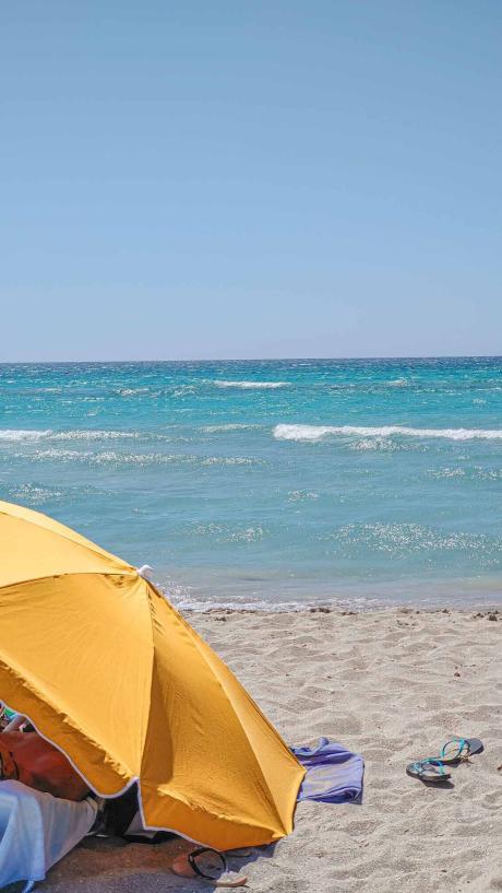 türkises Meer mit kleinen Wellen und einem orangen Sonnenschrim am Strand - Camping in Apulien