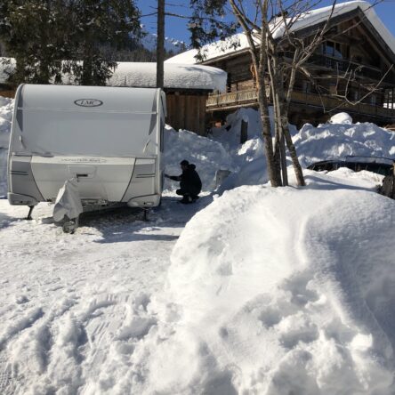 Wohnwagen im Schnee auf dem Campingplatz , blauer Himmel, Berge im Hintergrund